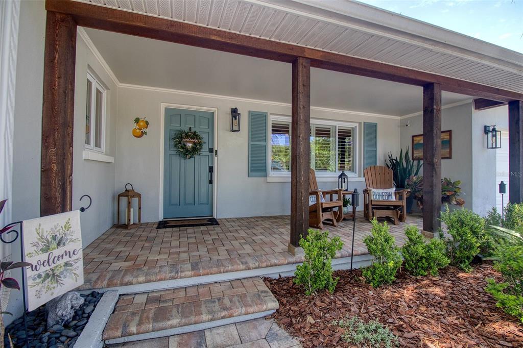 A covered front porch features a blue door, wooden columns, and brick paver flooring — 128 EDGEWATER TERRACE, DUNEDIN, FL