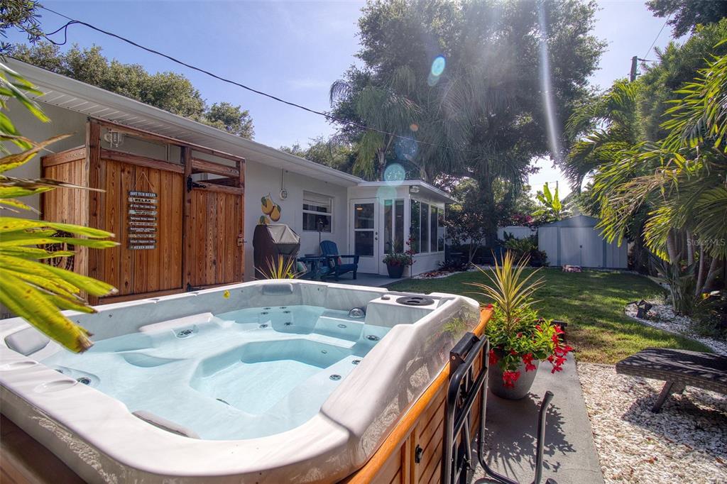 A backyard features a hot tub on a patio next to a house and lawn — 128 EDGEWATER TERRACE, DUNEDIN, FL