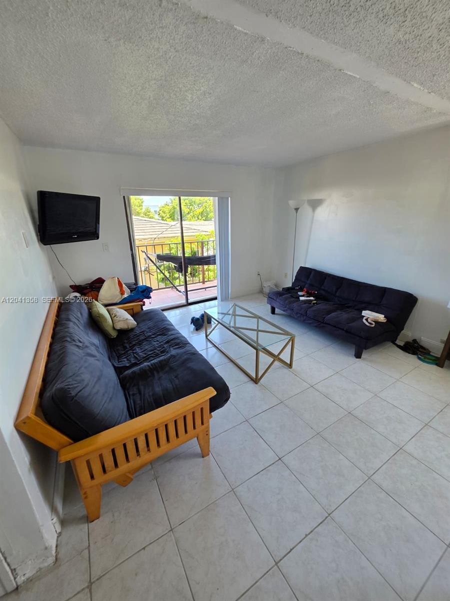 A living room features two futons, a glass coffee table, and a sliding glass door — 990 Biarritz Dr # 303, Miami Beach FL 33141, MIAMI BEACH, FL