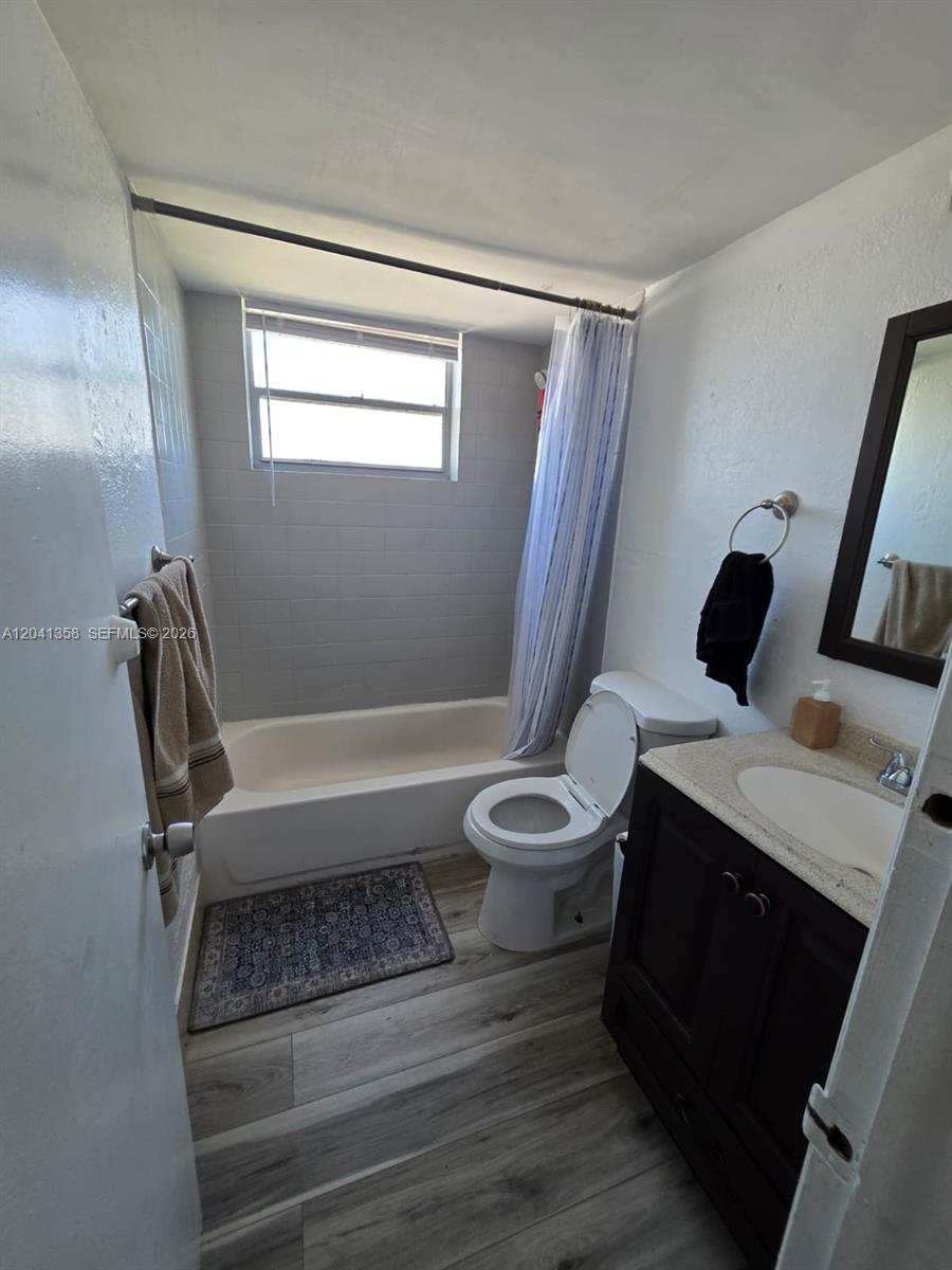 A bathroom features a bathtub with a shower curtain, a toilet, and a vanity sink — 990 Biarritz Dr # 303, Miami Beach FL 33141, MIAMI BEACH, FL