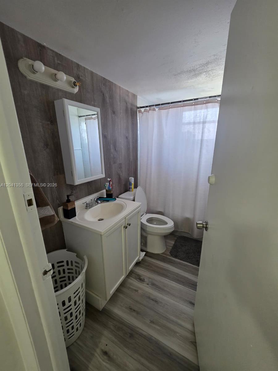 A bathroom features a white vanity, a wood-look accent wall, and a shower curtain — 990 Biarritz Dr # 303, Miami Beach FL 33141, MIAMI BEACH, FL