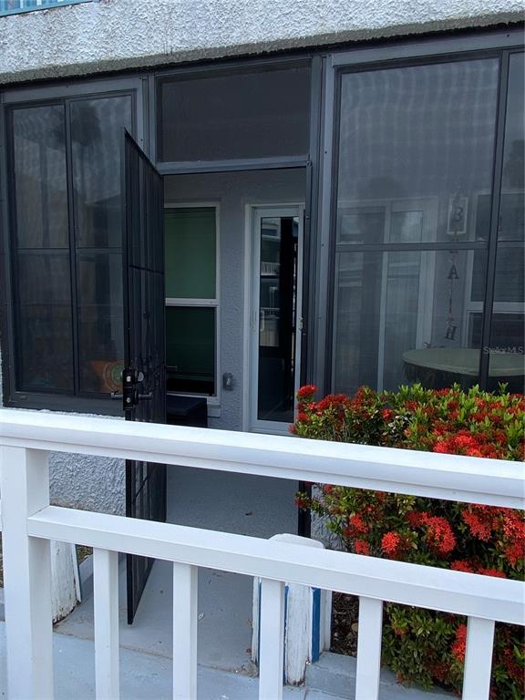A screened-in porch features a dark metal security door and a white wooden railing — 230 MEDALLION BOULEVARD UNIT D, MADEIRA BEACH, FL