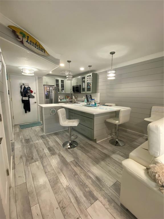 A kitchen features a white island with bar stools, gray shiplap walls, and wood-look flooring — 230 MEDALLION BOULEVARD UNIT D, MADEIRA BEACH, FL