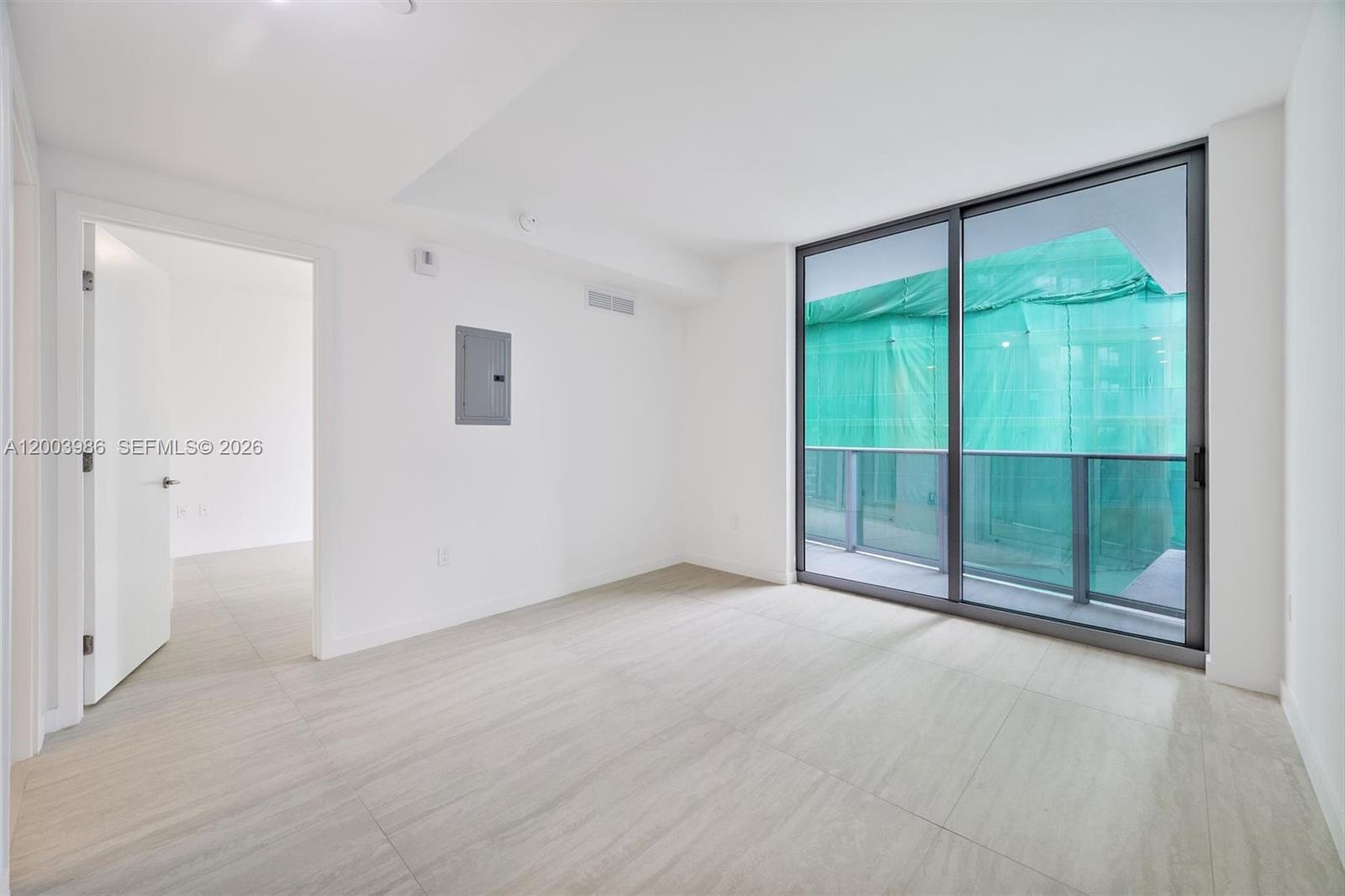 An empty room with light tile flooring, a doorway, and a balcony with green construction netting — 77 SE 5th Street # 3005, Miami FL 33131, MIAMI, FL