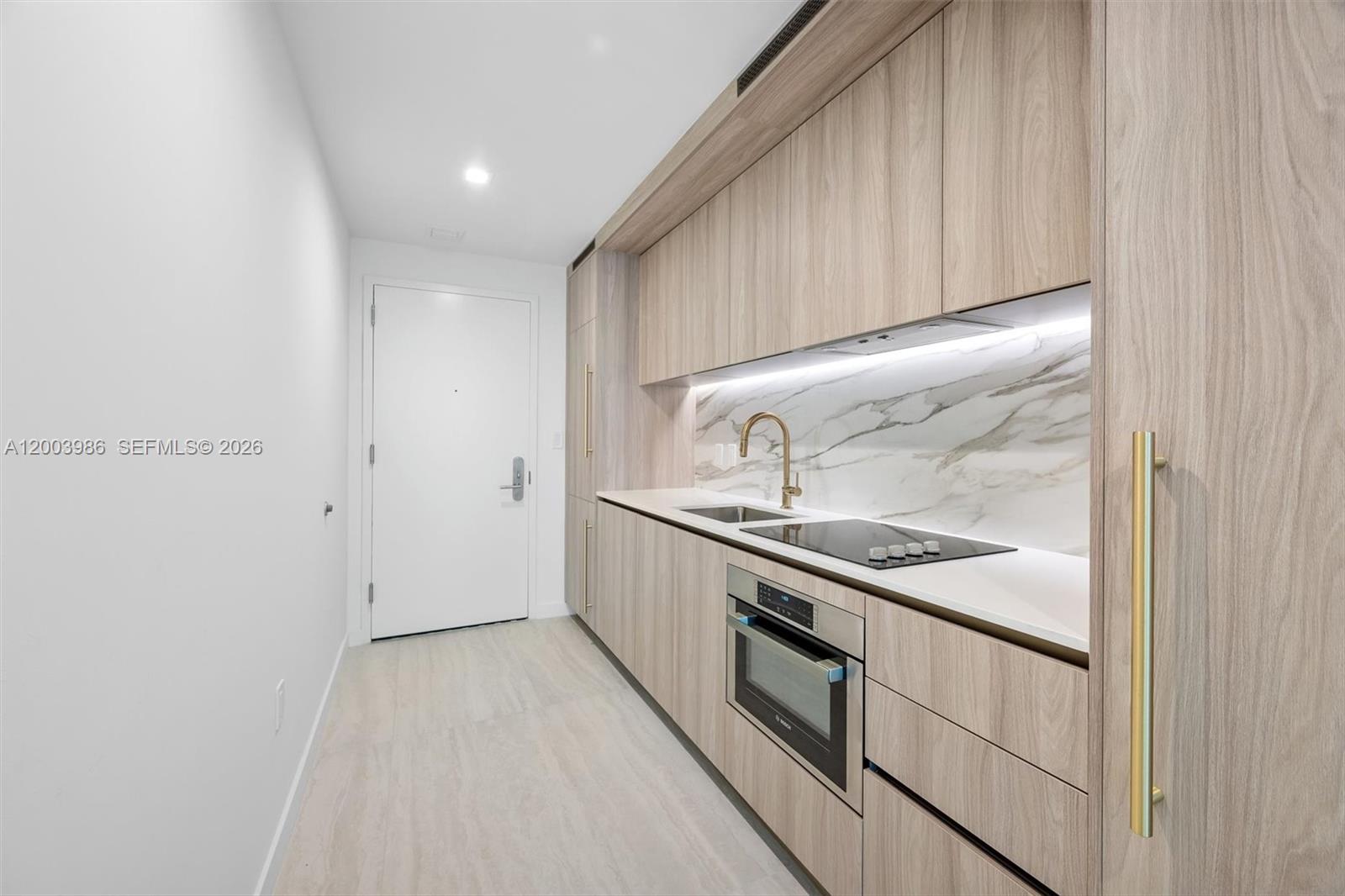 A modern kitchen features light wood cabinetry, a marble backsplash, and stainless steel appliances — 77 SE 5th Street # 3005, Miami FL 33131, MIAMI, FL