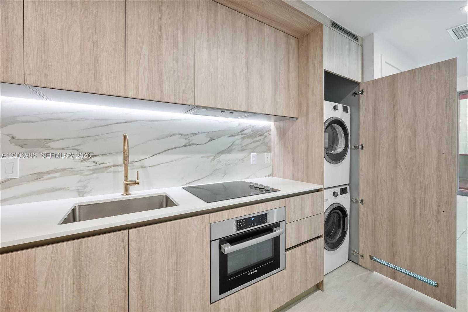 A modern kitchen features light wood cabinetry, a marble backsplash, and a stacked laundry unit — 77 SE 5th Street # 3005, Miami FL 33131, MIAMI, FL
