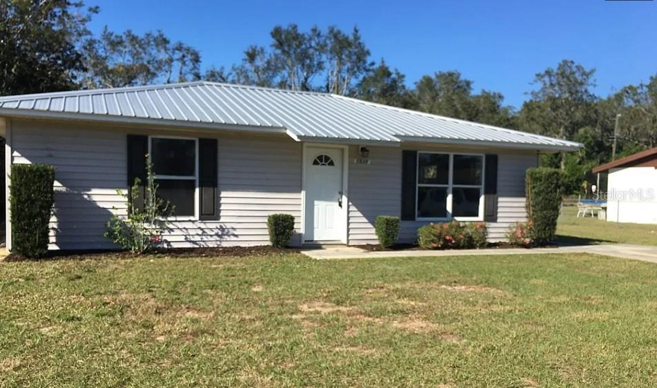 A single-story house with light gray siding and a metal roof sits on a lawn — 1539 PENNY AVENUE, SEBRING, FL