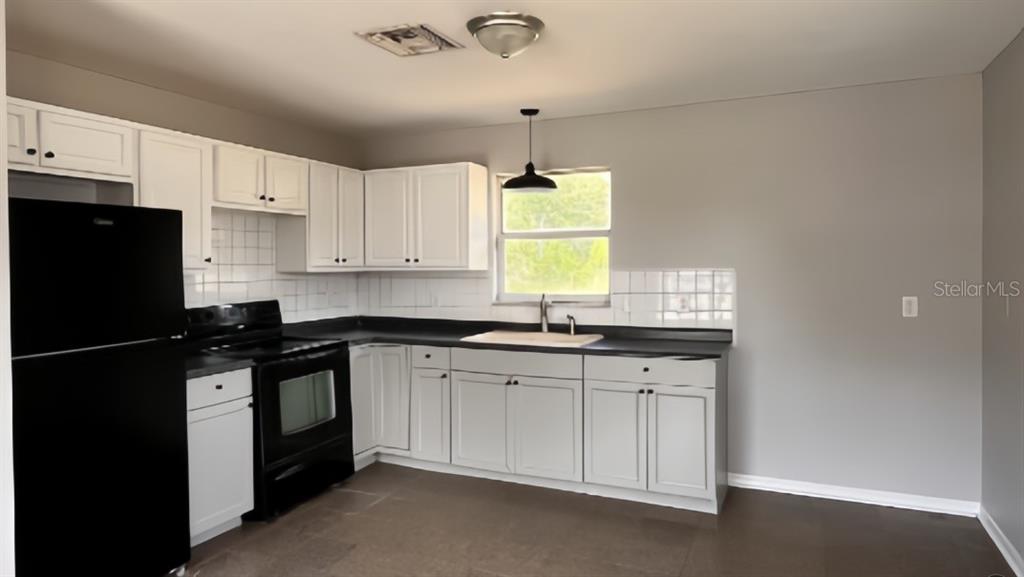 A kitchen features white cabinets, black appliances, a dark countertop, and a single window — 1539 PENNY AVENUE, SEBRING, FL