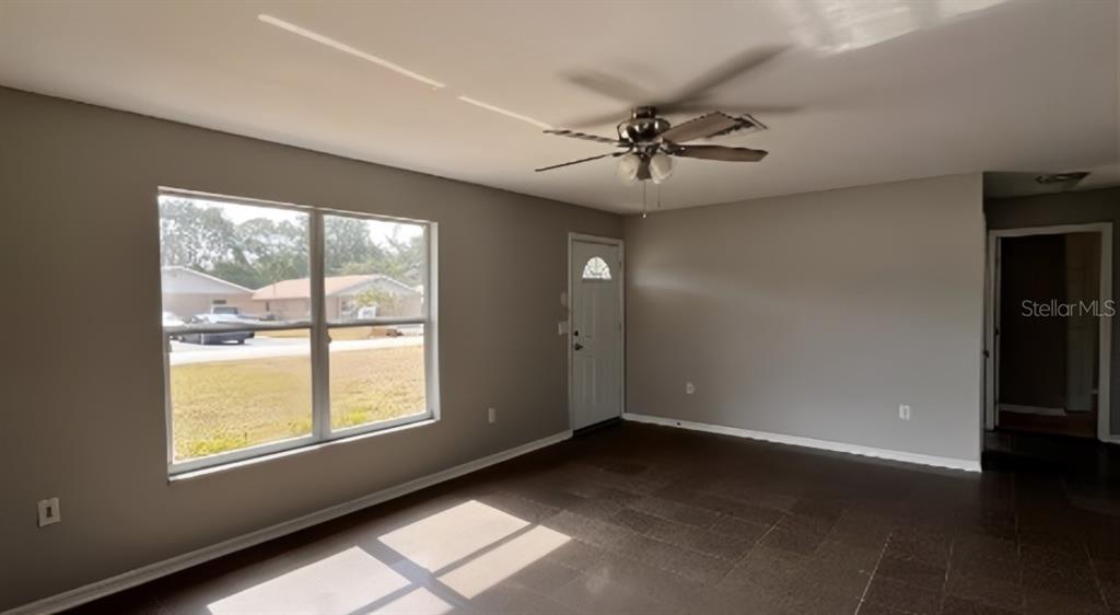 A living room with gray walls, dark tile flooring, a ceiling fan, and a window — 1539 PENNY AVENUE, SEBRING, FL