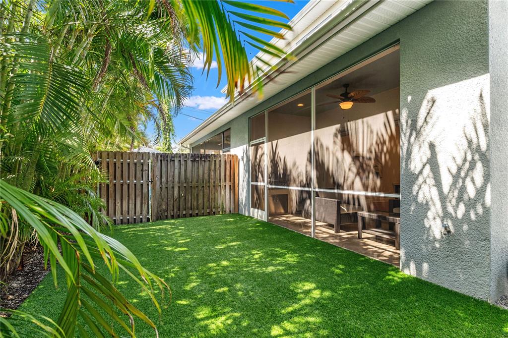 A small backyard with artificial turf, a wooden fence, and a screened-in patio area — 606 S LINCOLN AVENUE UNIT 2, TAMPA, FL
