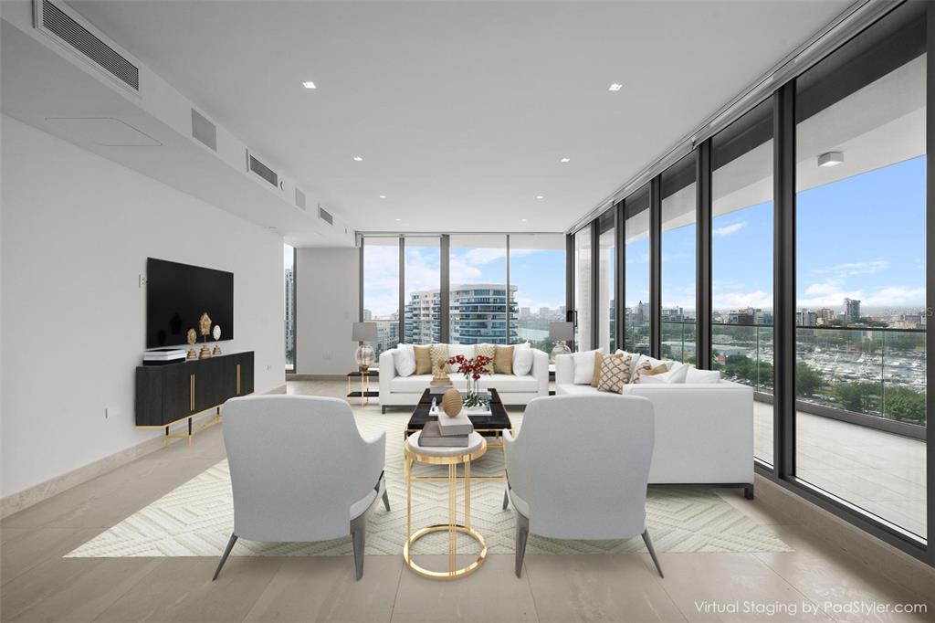 This virtual staging shows a modern living room with floor-to-ceiling windows overlooking a city skyline — 540 DE LA CONSTITUCION AVENUE UNIT 1202, SAN JUAN, PR