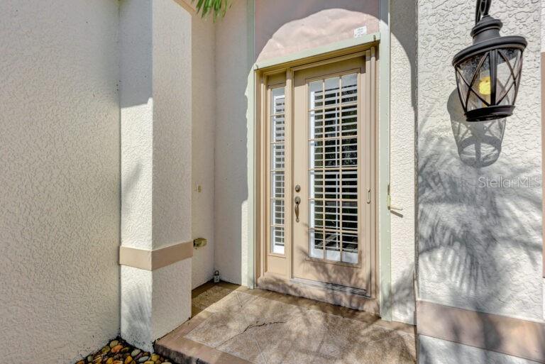 A beige front door with a glass insert and sidelight sits on a tiled porch — 13099 PRESERVE COURT, PORT CHARLOTTE, FL