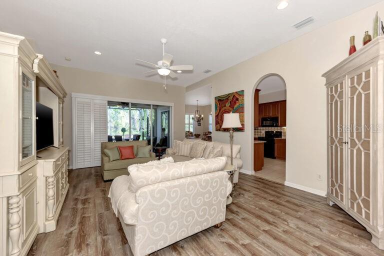 A living room features light wood-look flooring, a ceiling fan, and an arched kitchen doorway — 13099 PRESERVE COURT, PORT CHARLOTTE, FL