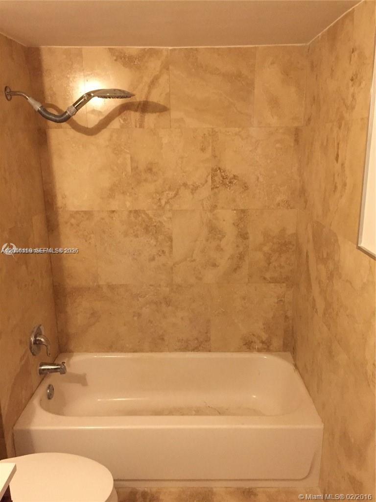 A white bathtub is set against a wall covered in tan stone tiles — 4110 NW 79th Ave # 1B, Doral FL 33166, DORAL, FL