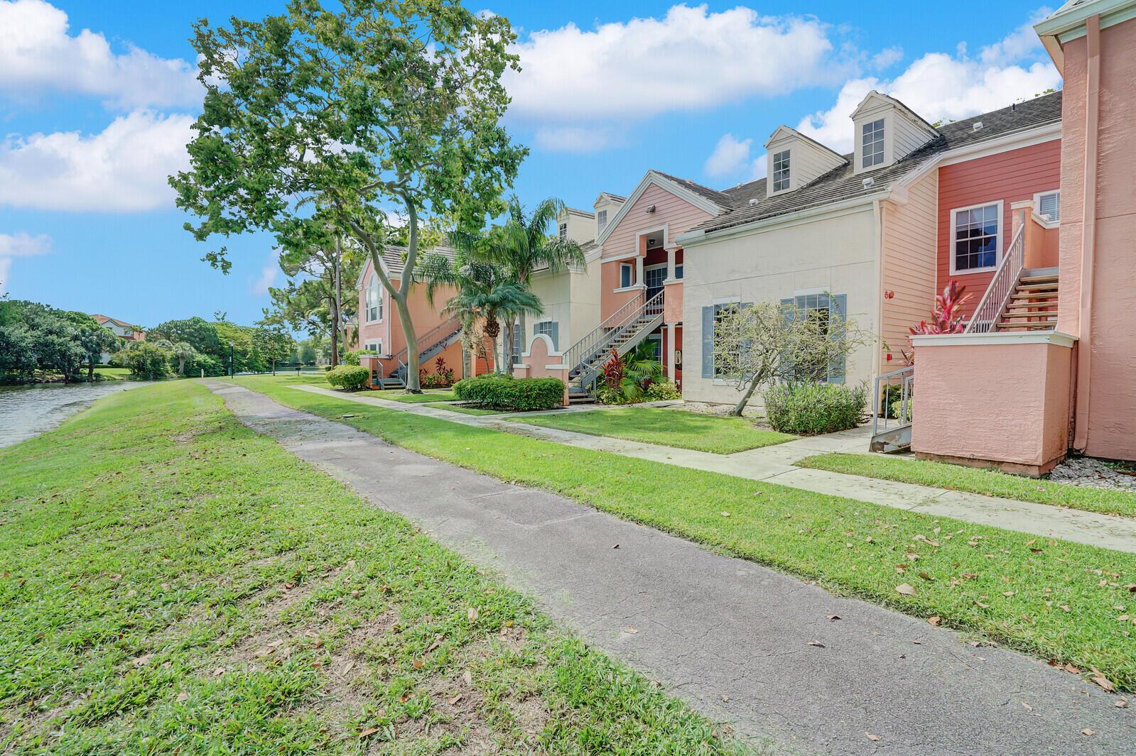 A paved path runs alongside a grassy lawn and multi-story apartment buildings near a lake — 1385 Crystal Way # M, Delray Beach FL 33444, DELRAY BEACH, FL