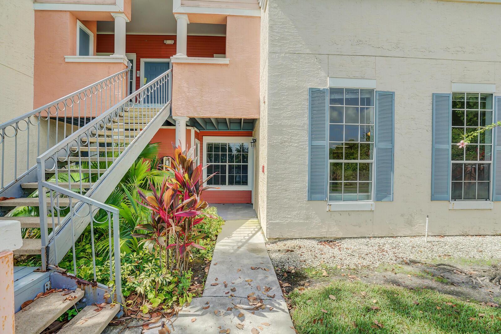 An exterior view of a multi-story building with a staircase, walkway, and blue-shuttered windows — 1385 Crystal Way # M, Delray Beach FL 33444, DELRAY BEACH, FL