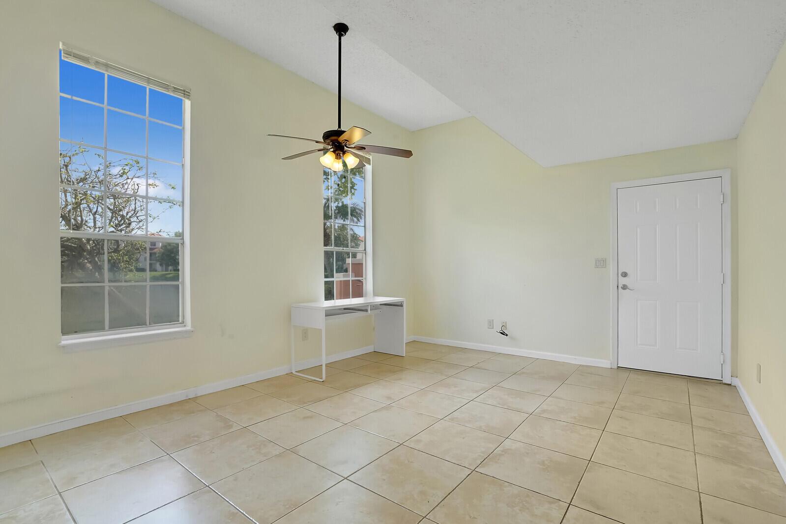 A room with beige tile floors, a ceiling fan, two windows, and a white door — 1385 Crystal Way # M, Delray Beach FL 33444, DELRAY BEACH, FL