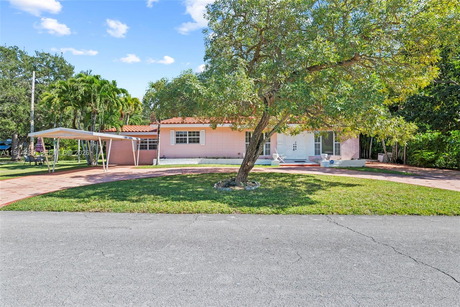 A pink, single-story house with a tile roof and a carport sits behind a tree — 700 NE 118th St, Biscayne Park FL 33161, BISCAYNE PARK, FL