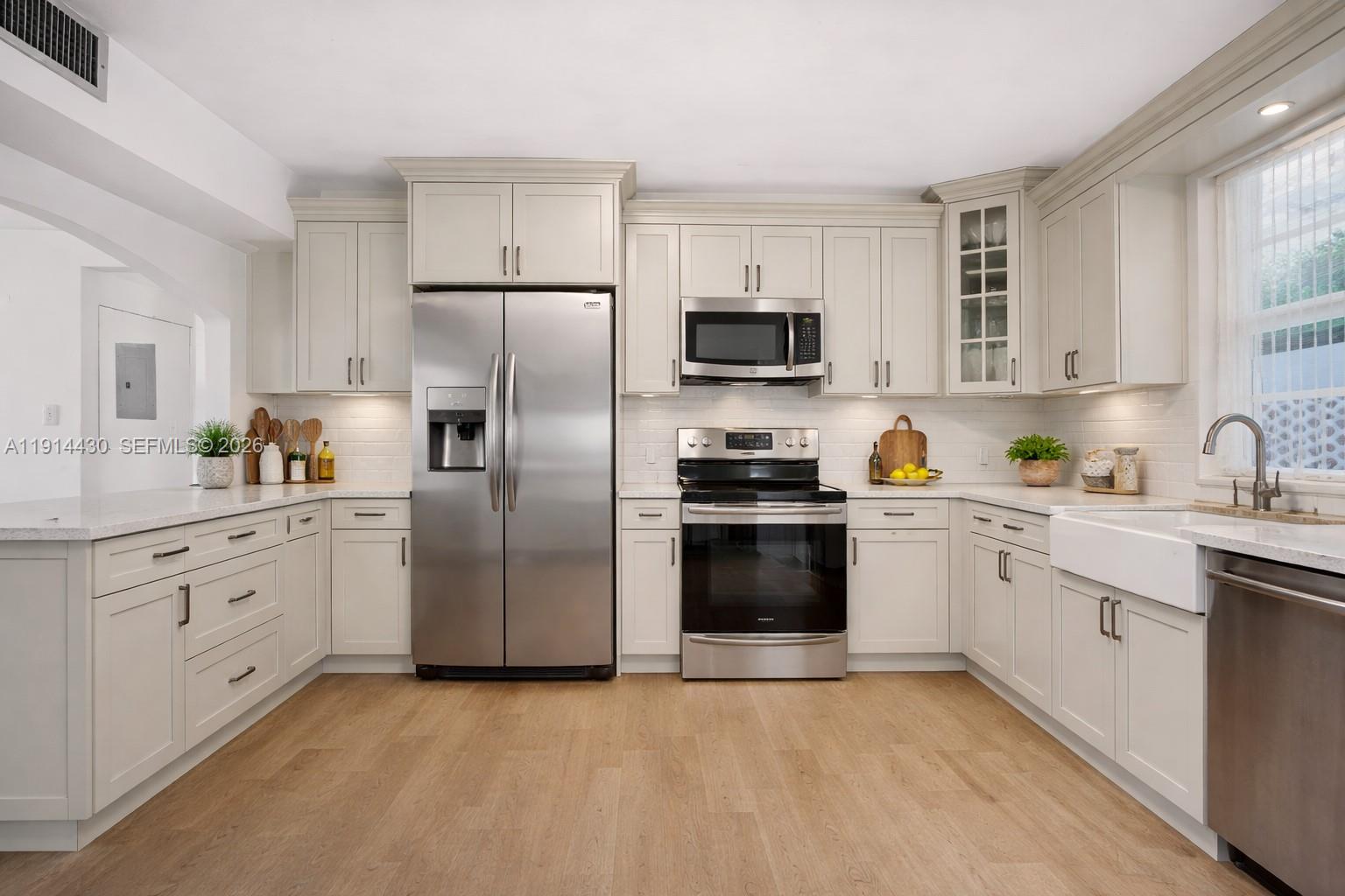 A modern kitchen features light-colored cabinetry, stainless steel appliances, and light wood flooring — 700 NE 118th St, Biscayne Park FL 33161, BISCAYNE PARK, FL