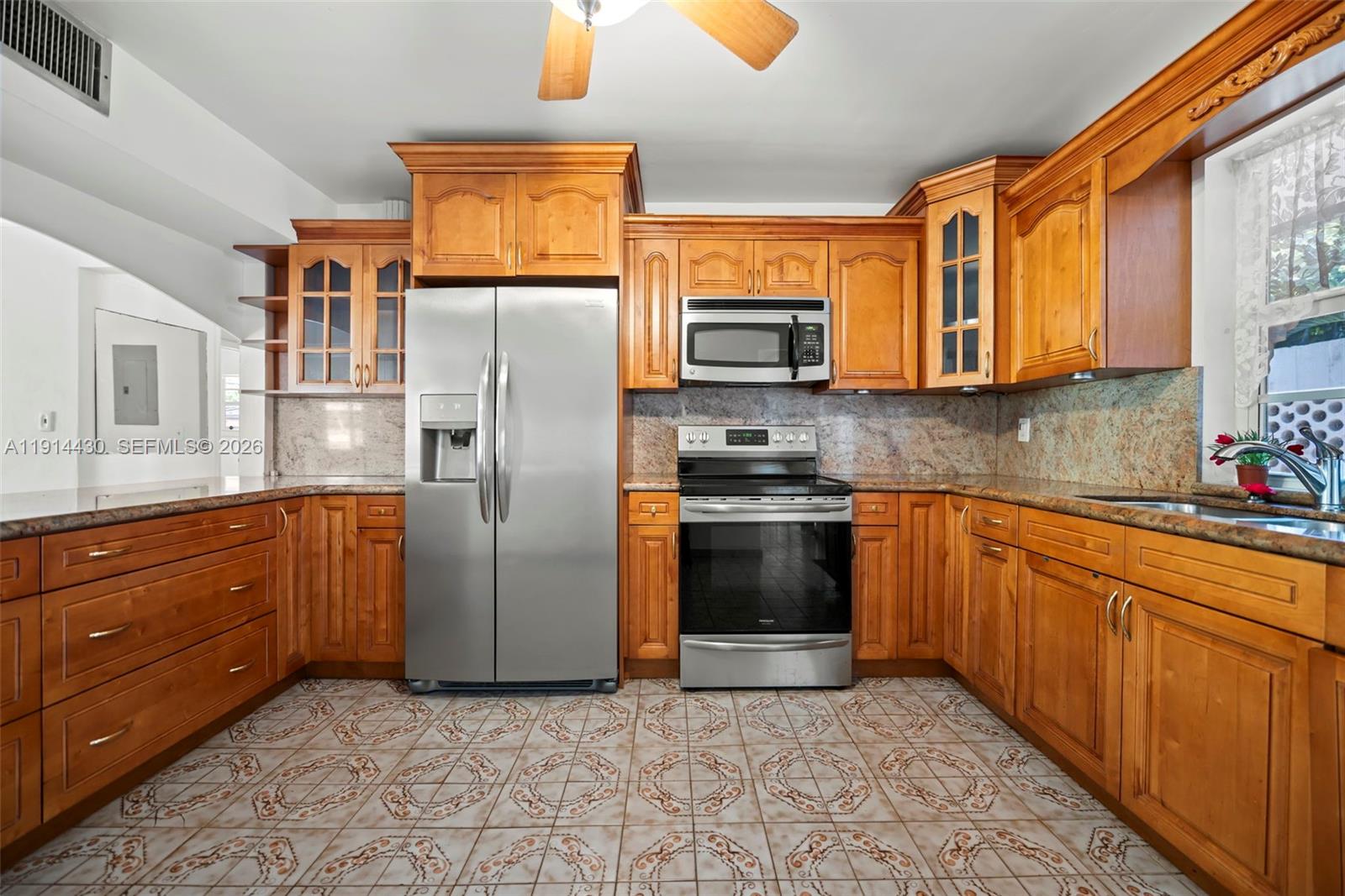 A kitchen features wooden cabinets, stainless steel appliances, granite countertops, and patterned tile flooring — 700 NE 118th St, Biscayne Park FL 33161, BISCAYNE PARK, FL