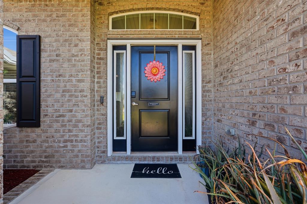 A black front door with a floral wreath and a hello doormat on a brick porch — 120 BREN MAR LANE, PALM COAST, FL