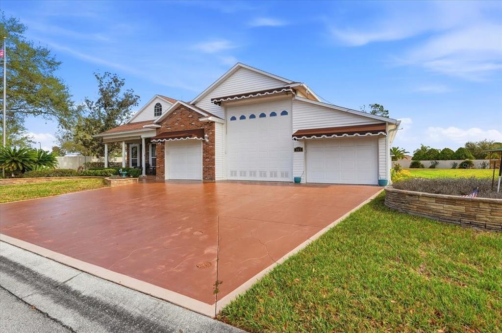 A house exterior features a large concrete driveway, three garage doors, and brick accents — 305 MOTORCOACH DRIVE S, POLK CITY, FL