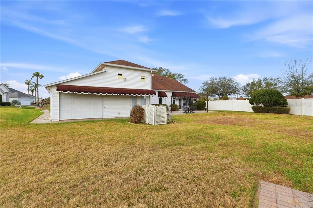 The exterior of a white house features a garage, a brown awning, and a large yard — 305 MOTORCOACH DRIVE S, POLK CITY, FL