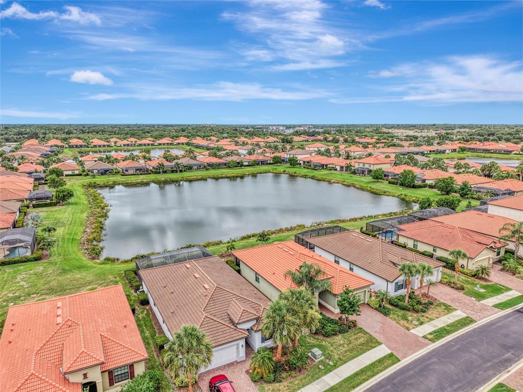 An aerial view shows suburban houses with tile roofs surrounding a central retention pond — 9903 WINGOOD DRIVE, VENICE, FL