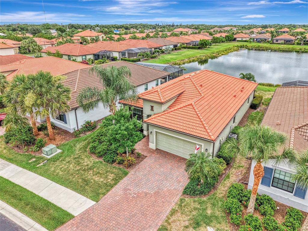 An aerial view shows a suburban house with a terracotta tile roof and brick driveway — 9903 WINGOOD DRIVE, VENICE, FL