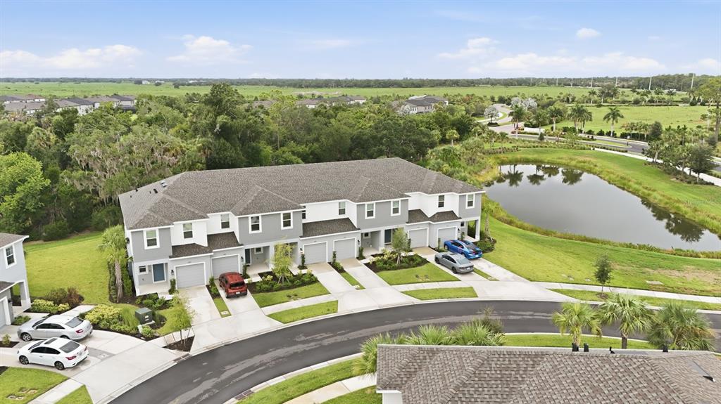 An aerial view shows a multi-unit townhouse building with gray siding and a pond nearby — 8417 LUNAR SKYE STREET, SARASOTA, FL