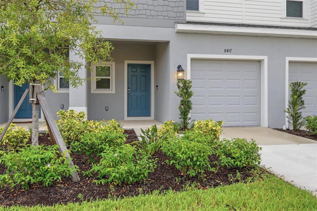 A gray townhome exterior features a blue front door, a garage, and landscaped front yard — 8417 LUNAR SKYE STREET, SARASOTA, FL