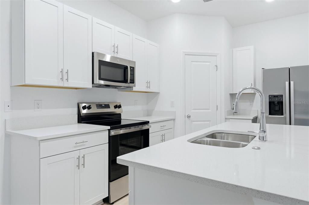 A modern kitchen features white cabinetry, stainless steel appliances, and a central island with sink — 8417 LUNAR SKYE STREET, SARASOTA, FL