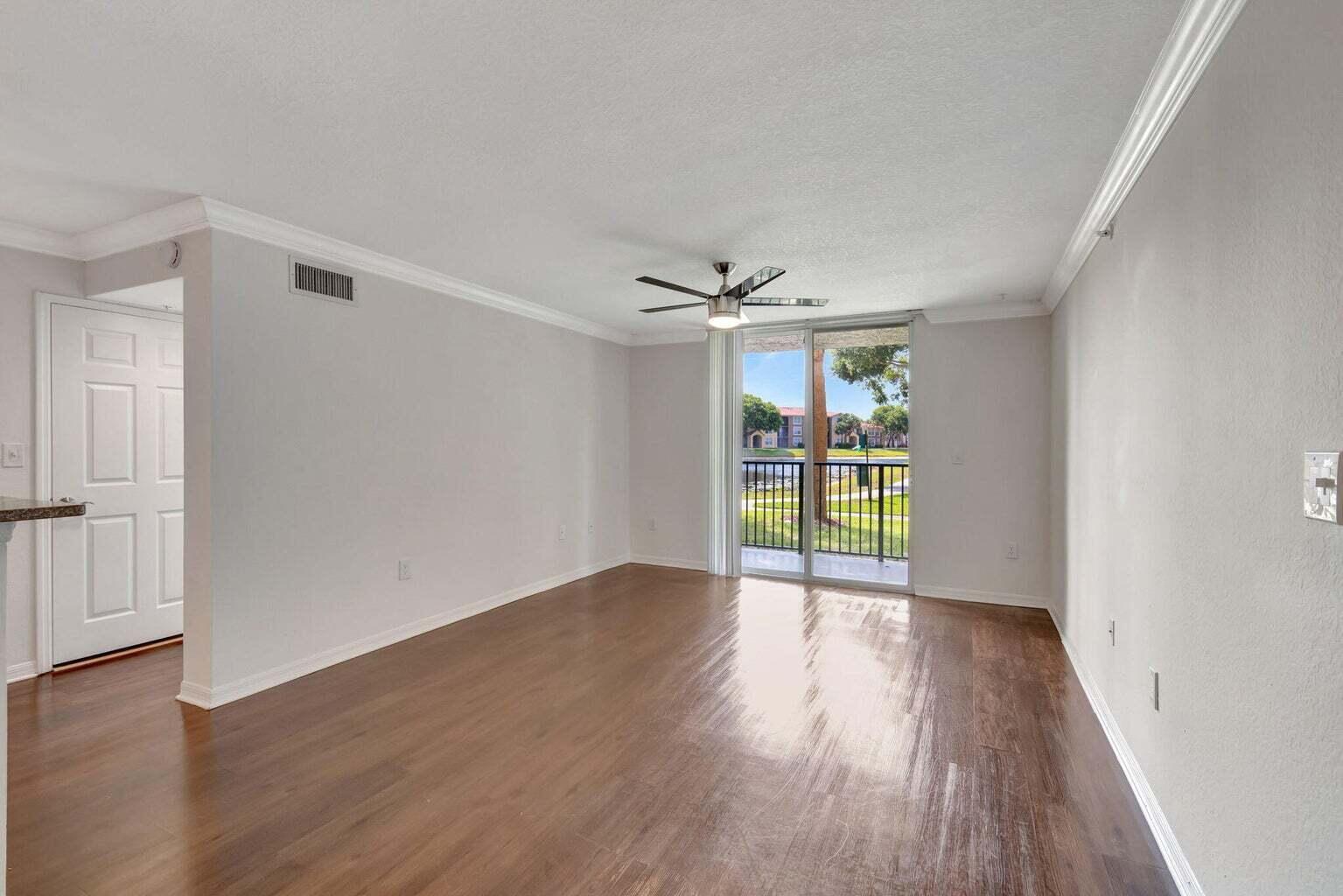 An empty living room features wood-look flooring, a ceiling fan, and a sliding glass door — 15155 Michelangelo Boulevard # 106, Delray Beach FL 33446, DELRAY BEACH, FL