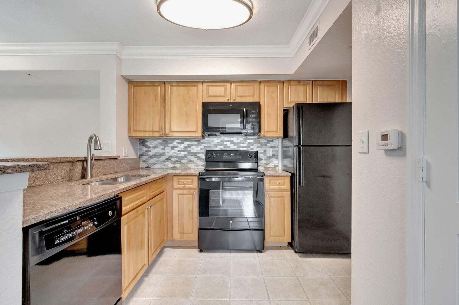 A kitchen with light wood cabinets, black appliances, granite countertops, and a patterned tile backsplash — 15155 Michelangelo Boulevard # 106, Delray Beach FL 33446, DELRAY BEACH, FL