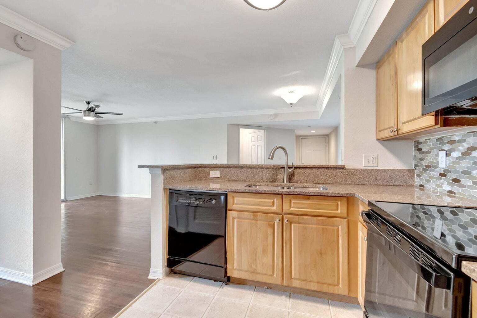A kitchen with light wood cabinets, granite countertops, and a black dishwasher overlooks an open living area — 15155 Michelangelo Boulevard # 106, Delray Beach FL 33446, DELRAY BEACH, FL