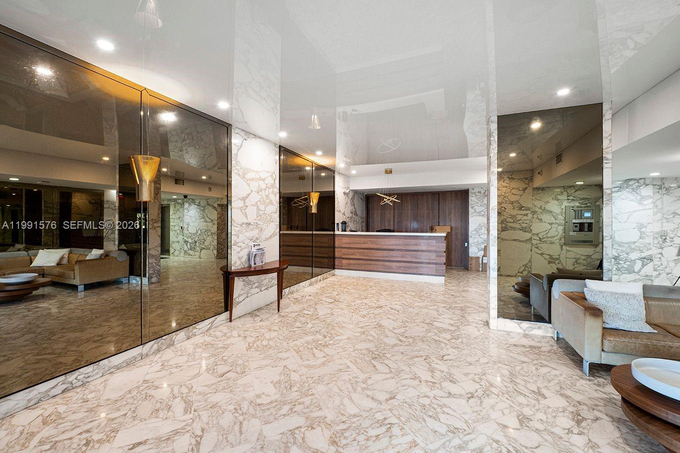 A modern lobby features marble floors and walls, mirrored panels, and a wooden reception desk — 7135 Collins Ave # 625, Miami Beach FL 33141, MIAMI BEACH, FL