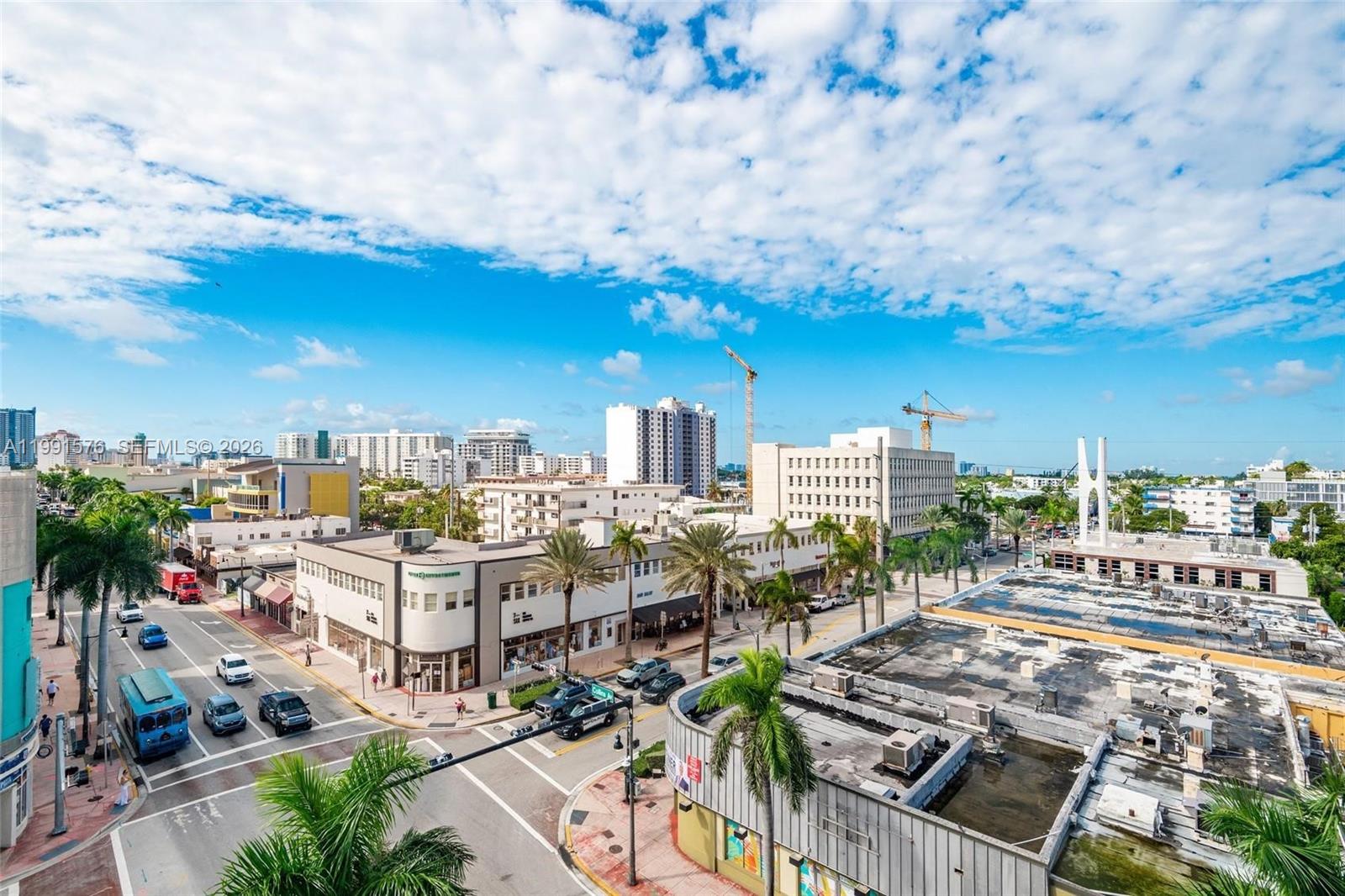 An elevated view of a city street intersection with palm trees, buildings, and construction cranes — 7135 Collins Ave # 625, Miami Beach FL 33141, MIAMI BEACH, FL