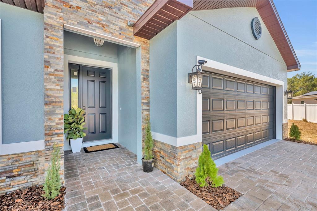 The exterior of a house features a stone-accented facade, a gray front door, and pavers — 256 HIBISCUS LANE, POINCIANA, FL