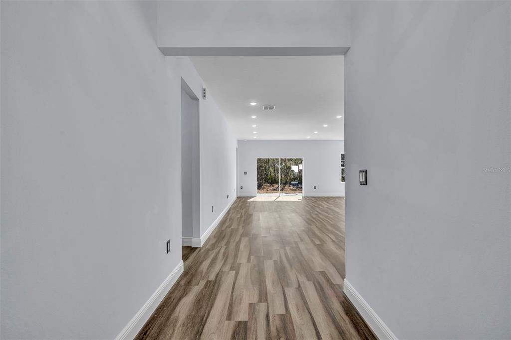 A bright, empty living area features light wood-look flooring and a sliding glass door — 256 HIBISCUS LANE, POINCIANA, FL