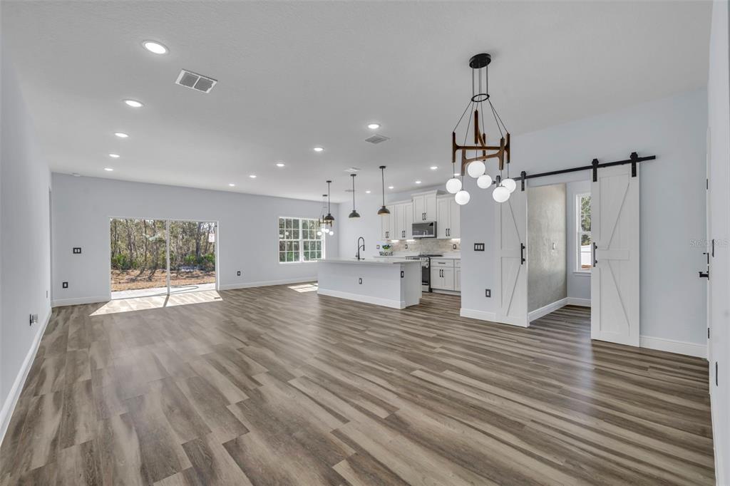 An open-concept kitchen and living area with wood-look flooring, white cabinetry, and a sliding door — 256 HIBISCUS LANE, POINCIANA, FL