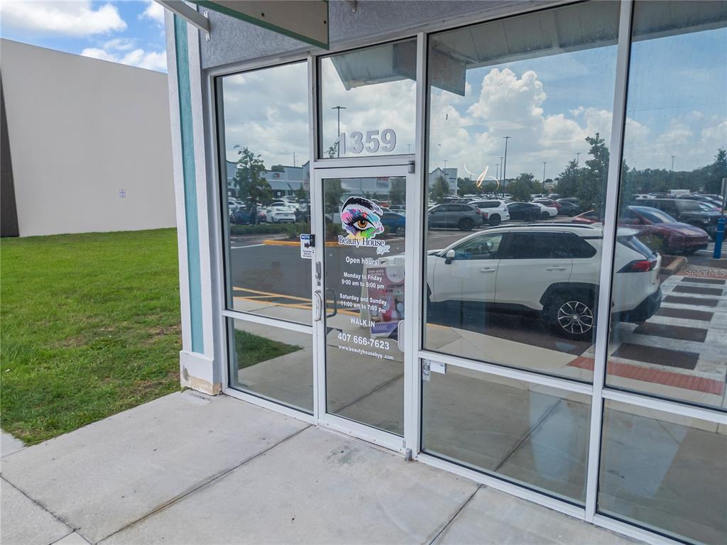 The exterior of a commercial storefront features a glass door with business hours and signage — 1359 E OSCEOLA PARKWAY, KISSIMMEE, FL