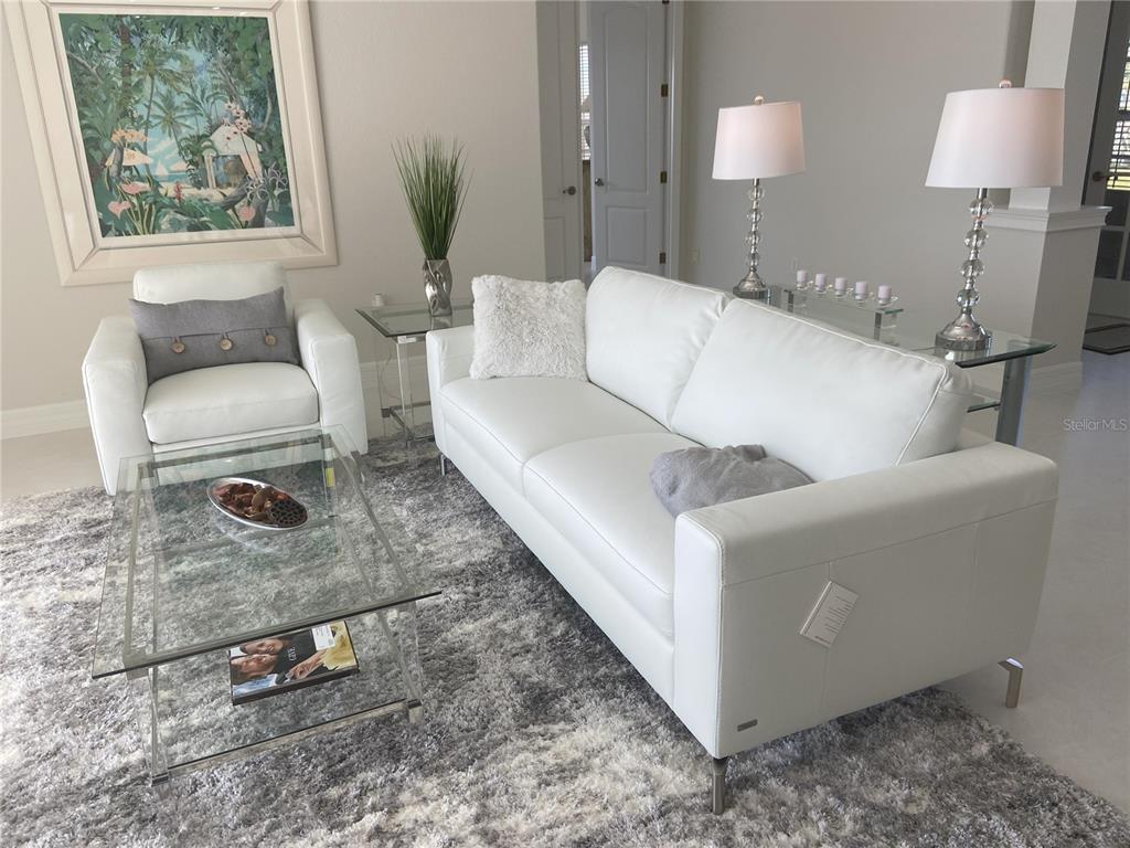 A living room features a white sofa, matching armchair, glass tables, and a gray rug — 3840 RUDDER WAY, NEW PORT RICHEY, FL
