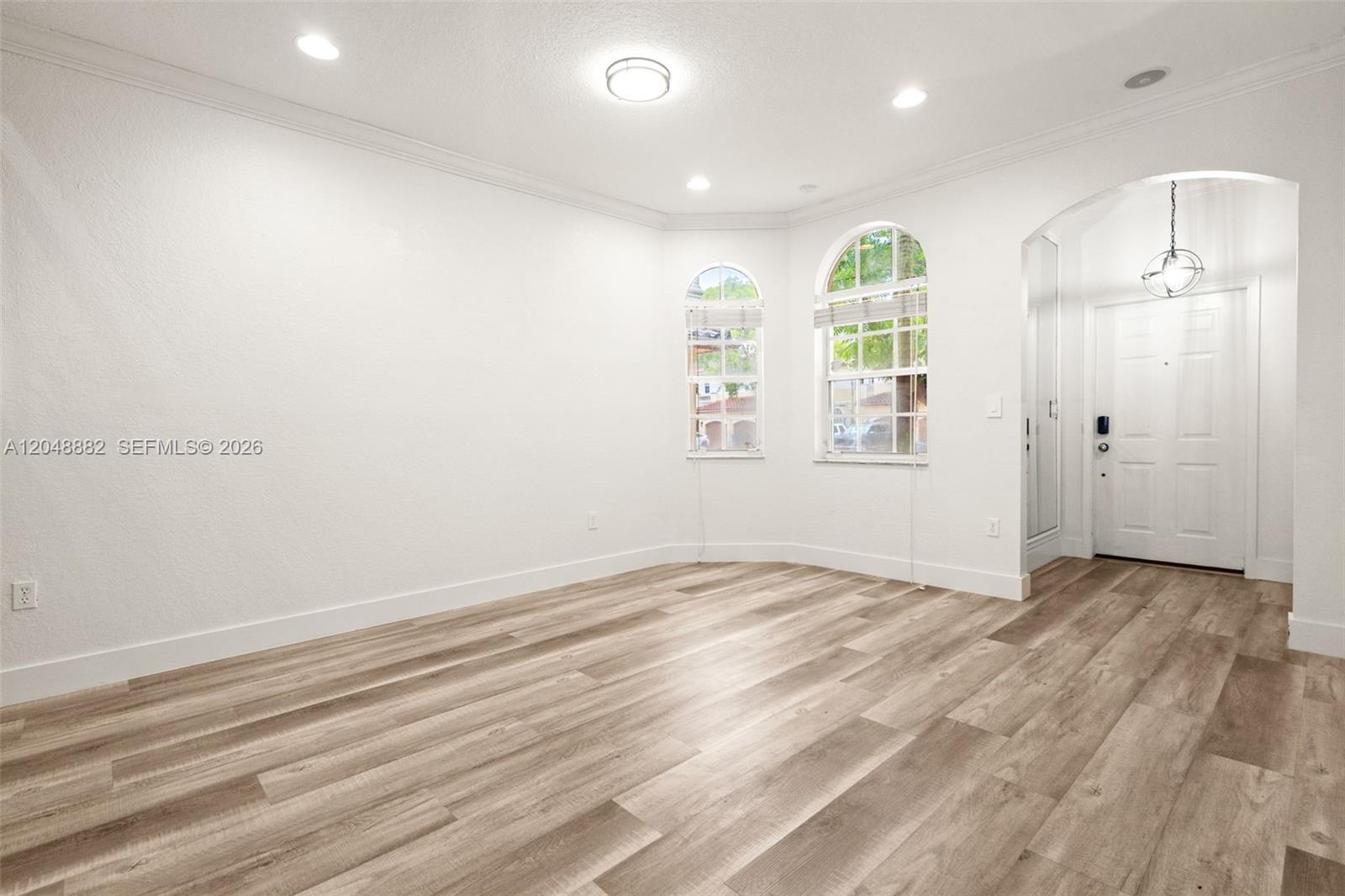 An empty room features light wood-look flooring, white walls, arched windows, and a recessed entryway — 4939 SW 136th Ave, Miramar FL 33027, MIRAMAR, FL