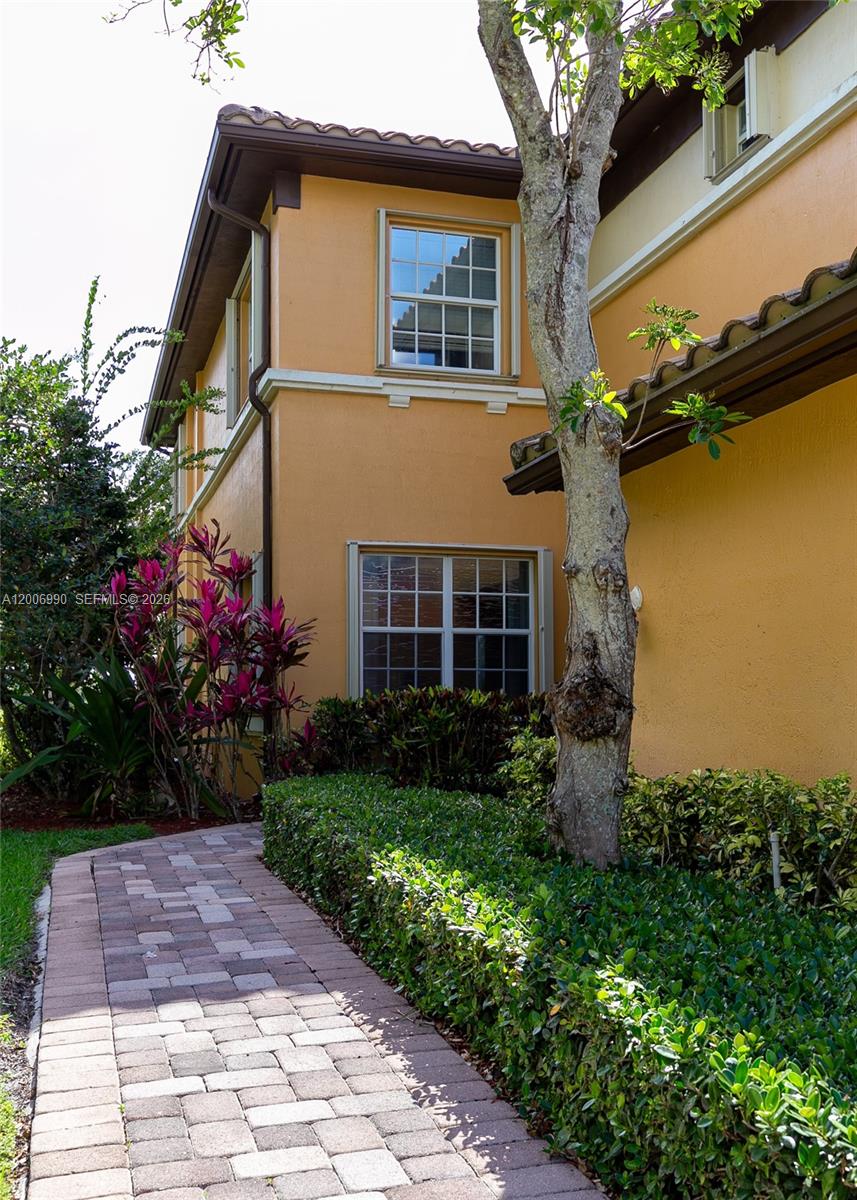 The exterior of a yellow stucco house features a white garage door and landscaping — 7901 NW 128th Ln # A, Parkland FL 33076, PARKLAND, FL