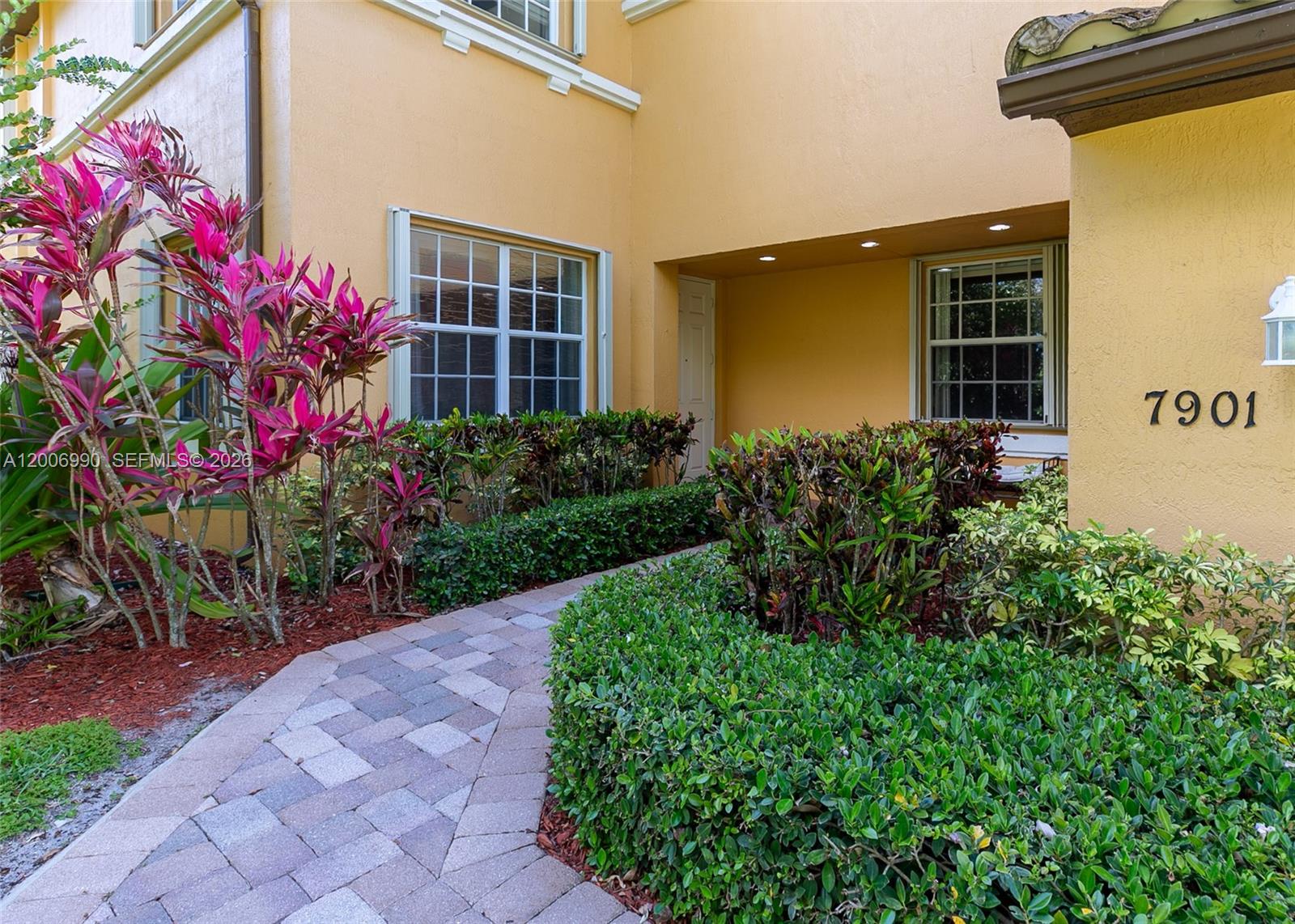 A paved walkway leads to the side of a two-story yellow stucco house — 7901 NW 128th Ln # A, Parkland FL 33076, PARKLAND, FL