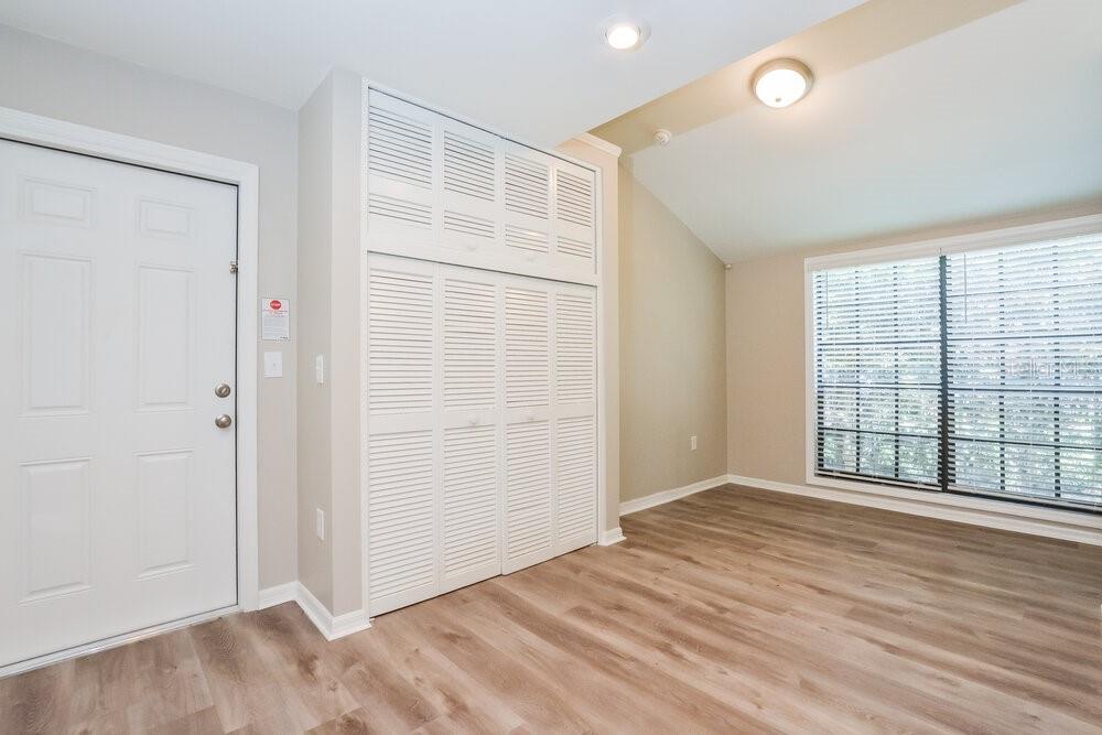 A room with light wood-look flooring, white louvered closet doors, and a large window — 51 DOGWOOD LANE, EUSTIS, FL
