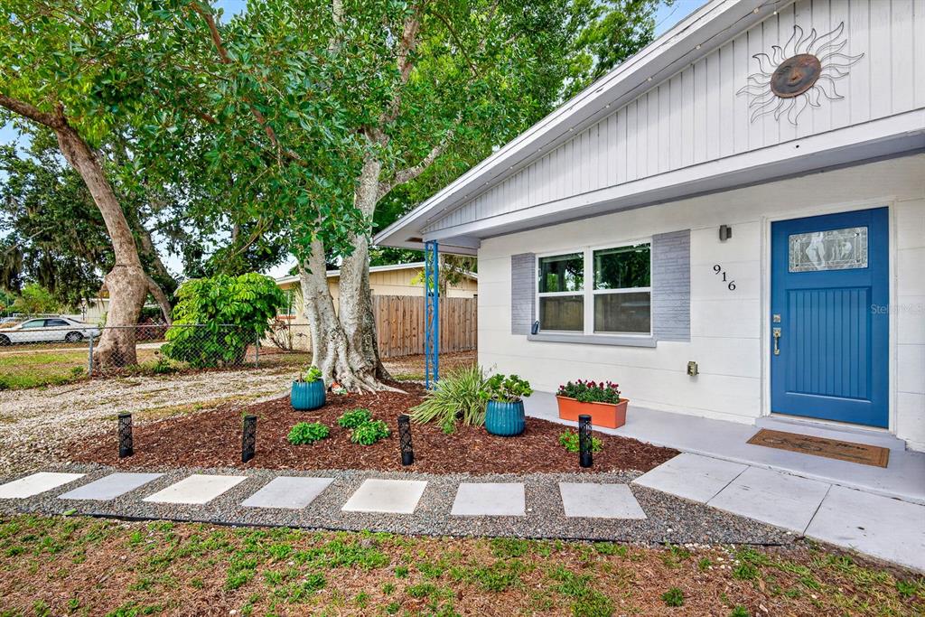 A white house exterior features a blue front door, a sun wall decoration, and landscaping — 916 PATTISON AVENUE, SARASOTA, FL
