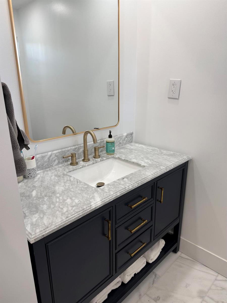 A bathroom vanity features a marble countertop, dark cabinetry, brass hardware, and a gold-framed mirror — 1511 Seabrook Road, Jupiter FL 33469, JUPITER, FL
