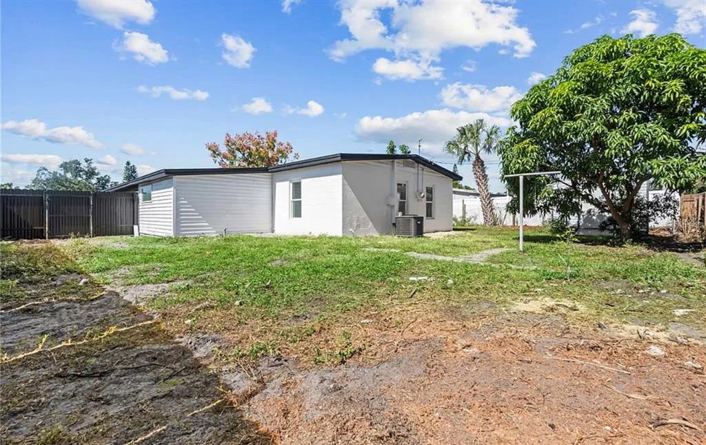 The exterior of a white, single-story house features a large backyard with a mature tree — 5101 TOWN N COUNTRY BOULEVARD, TAMPA, FL