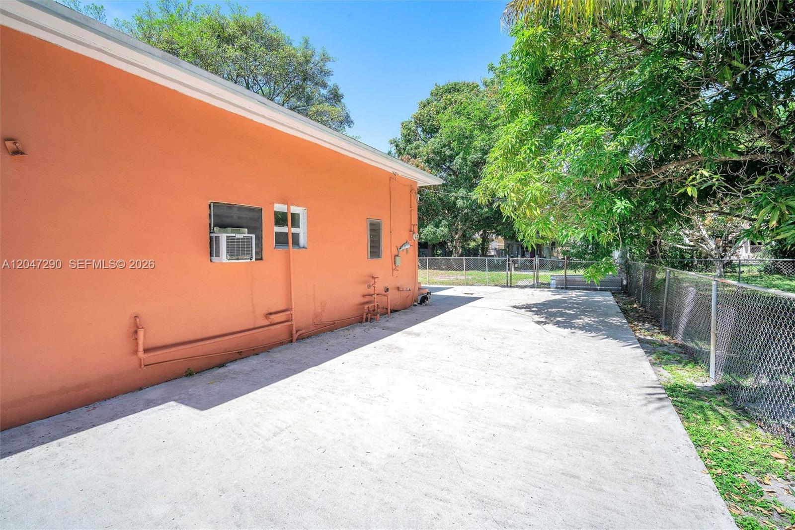 A concrete patio runs alongside the exterior wall of an orange house with a chain-link fence — 13140 N Miami Ave # 1, Miami FL 33168, MIAMI, FL
